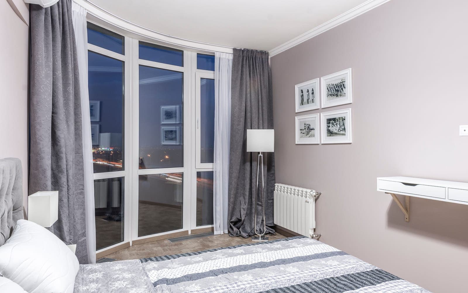 A bedroom with large windows looking out over a lit city street at night