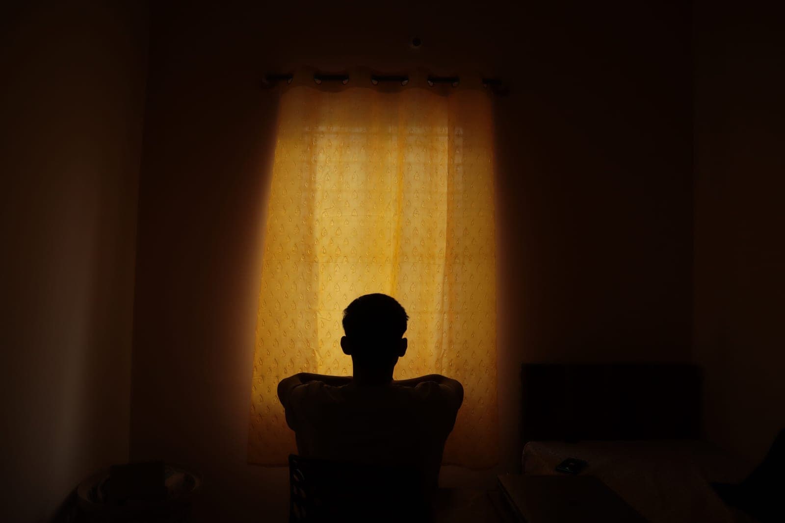 A dim bedroom with soft light around a covered window