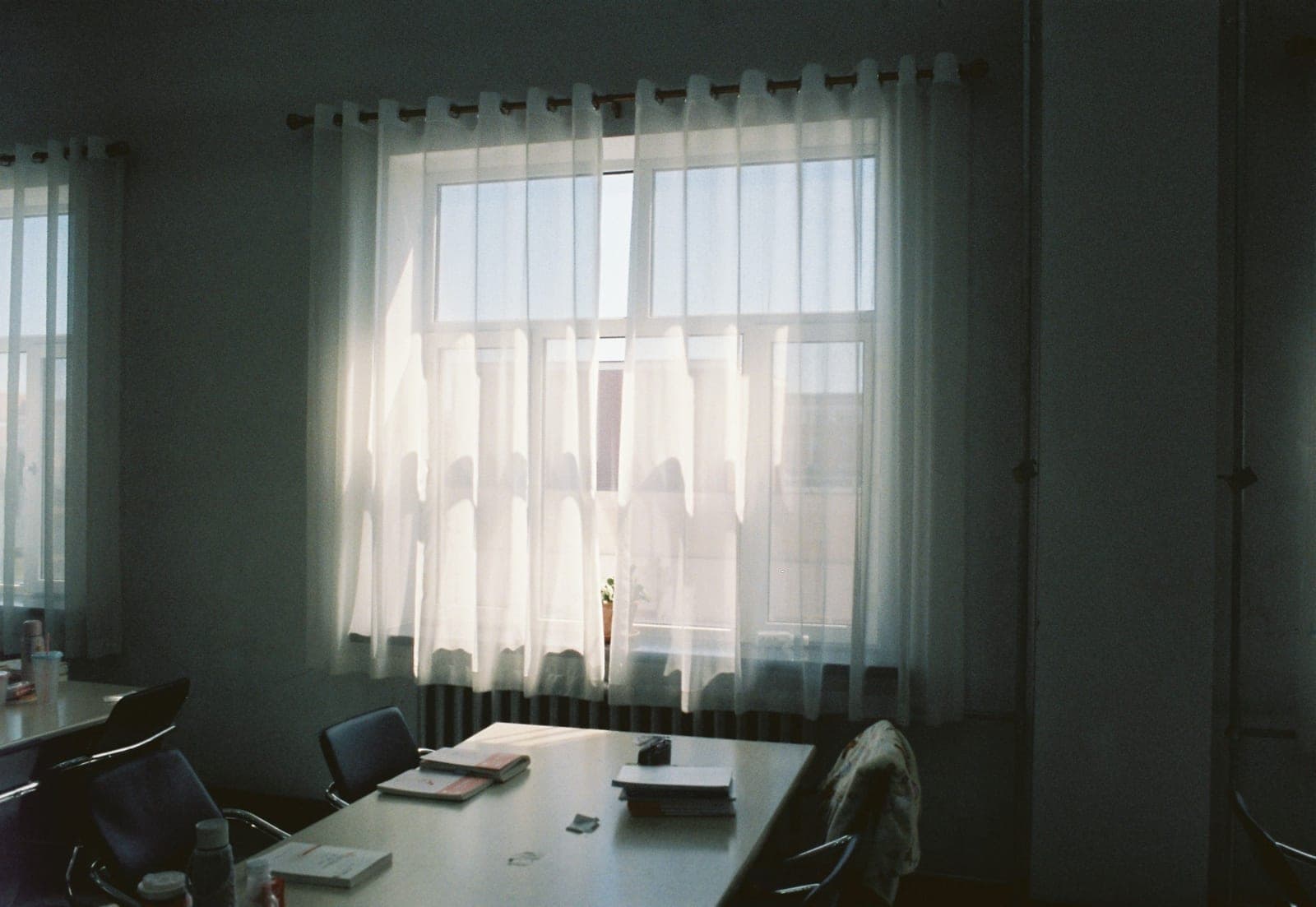 A desk beside a bright window with a sheer curtain diffusing the light