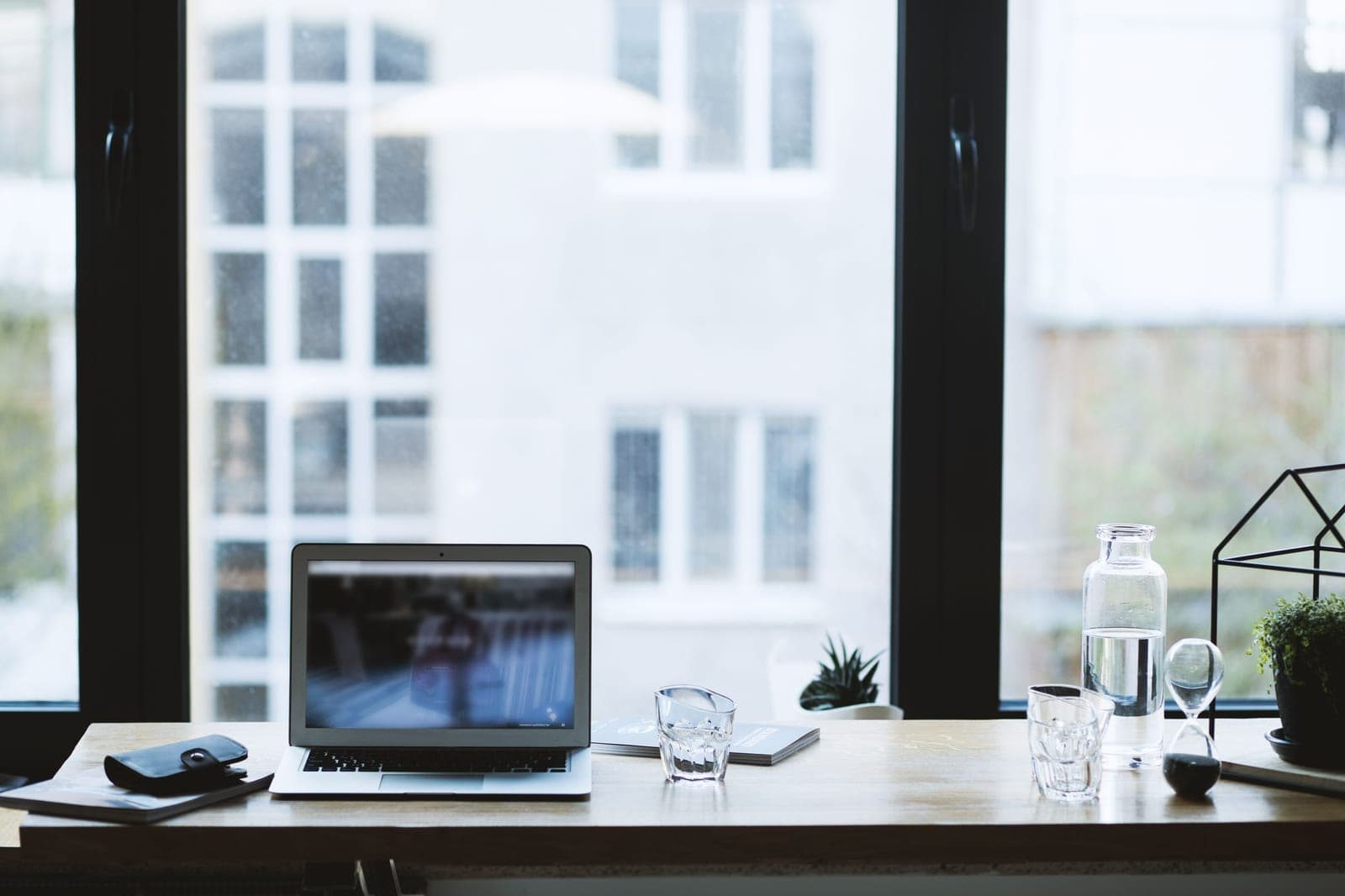 A home office desk with a laptop beside a window in daylight
