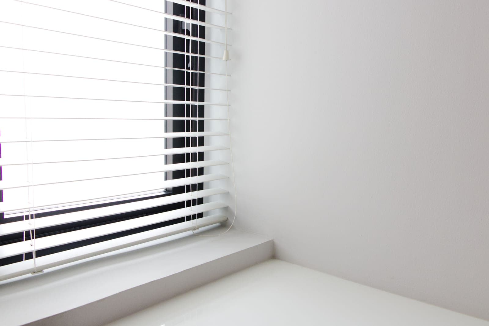 An apartment window with blinds partly closed above a city street