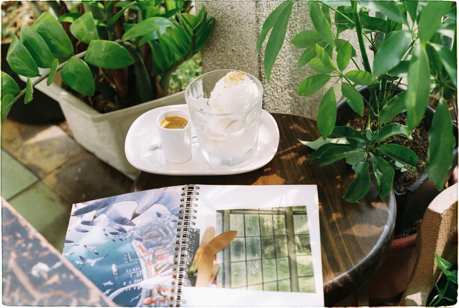 A notebook and a cup of coffee on a table beside a sunlit window